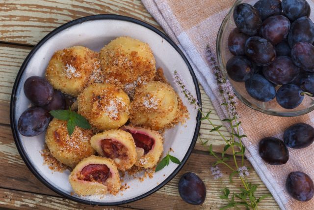 Sweet plum dumplings in metal bowl on wooden table